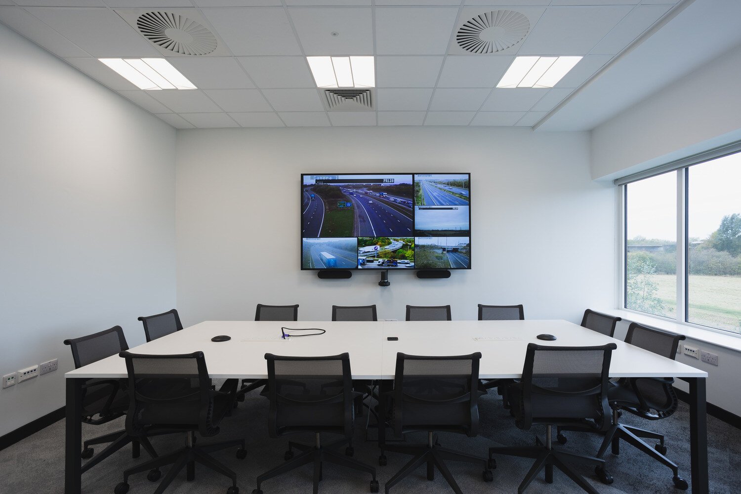 A screen on the wall and a desk with chairs in front of it