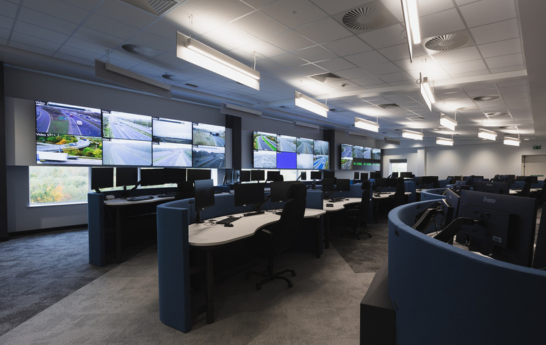 An angled view of the control room with monitors, desks and a video wall