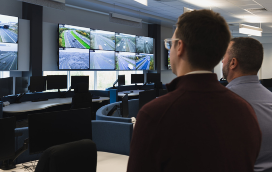 Two men looking at a wall of screens from afar