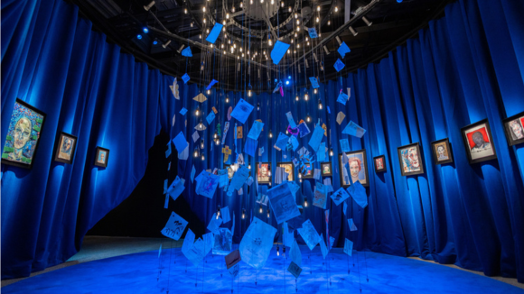 A curtain of relics hanging from the ceiling in a blue room with paintings hung on the wall